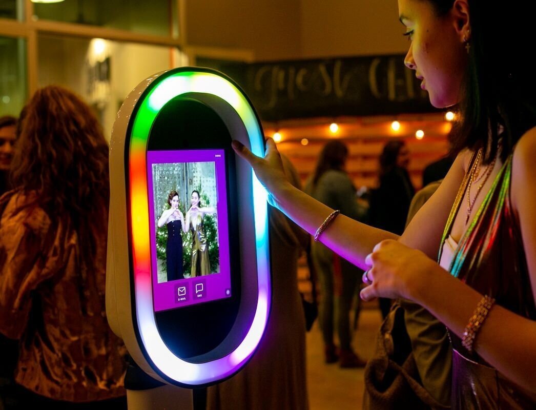Guest using a digital photo booth touchscreen with a rainbow LED ring light at an evening event