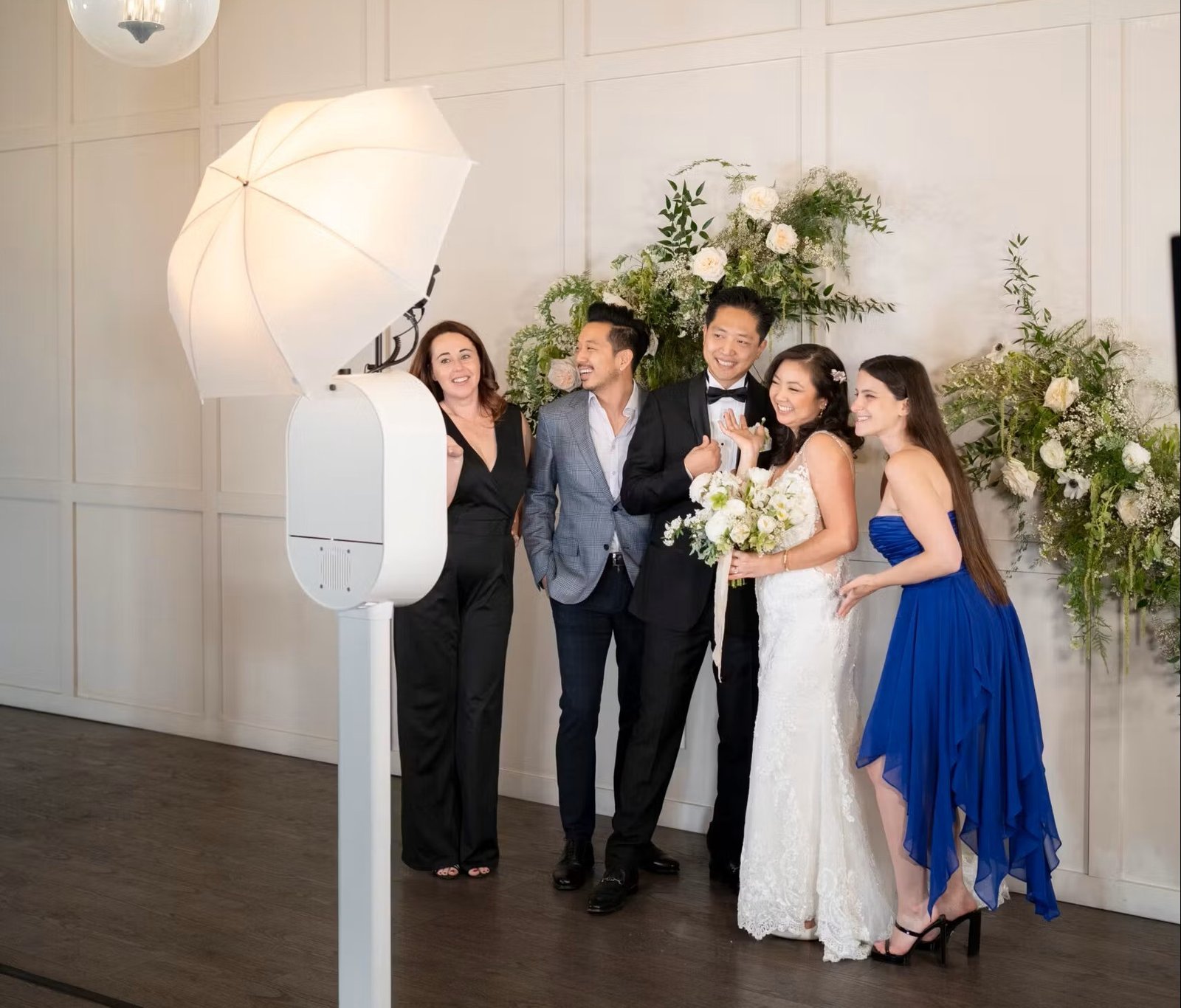 Wedding party posing at an open air photo booth with a white umbrella light and a floral backdrop